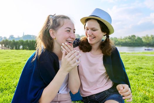 Girlfriends teenagers having fun while sitting on the grass on a sunny summer day, friendship adolescence vacation concept