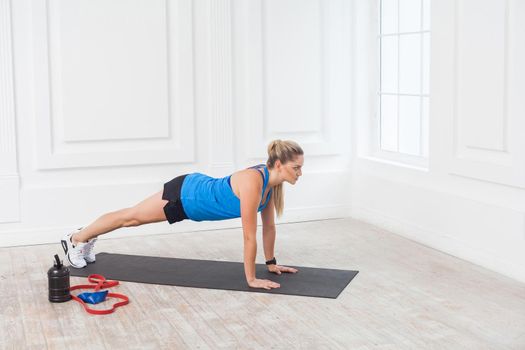 Side view of muscular sporty strong young beautiful athletic caucasian woman in black shorts and blue top standing on perfect plank position. Indoor, studio shot, sport and healthy concept