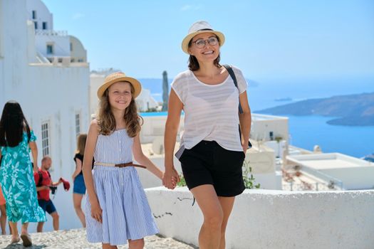 Happy tourists family mother and daughter kid walking on the Greek island of Santorini. Scenic marine and traditional architectural landscape background