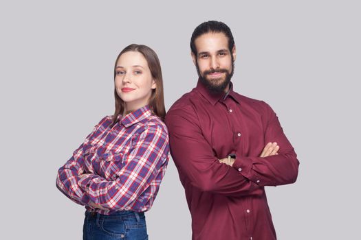 Portrait of satisfied bearded man with black collected hair and woman in casual style standing, smiling and looking at camera with crossed hands. indoor studio shot, isolated on gray background.