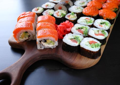 Top view of sushi rolls with salmon, cream cheese, caviar, chuka on a dark wooden cutting board. Fried sushi roll with salmon - japanese food. Sushi roll Philadelphia with salmon, smoked eel, avocado, cream cheese on a black background. Sushi menu. Selective focus