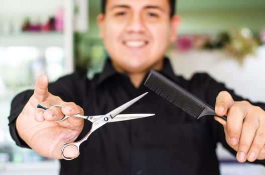 Portrait of an attractive barber holding scissors and comb in his hand