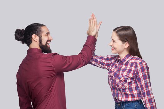 Profile side view of happy amazed bearded man with black collected hair and woman in casual style standing with fist and celebrating their victory. indoor studio shot, isolated on gray background.