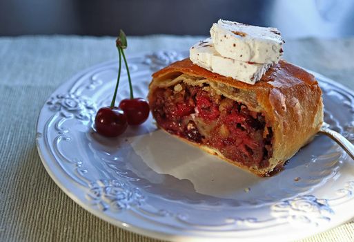 Sliced homemade strudel with cherries and a slice of ice cream, close-up on a white plate. Slice of freshly baked homemade strudel with cherries and walnuts