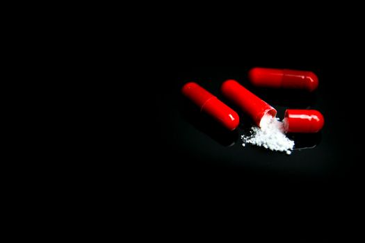 Open Red capsule with white medicine on black background
