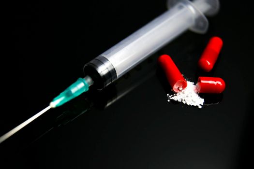 Open Red capsule with white medicine next to syringe on black background