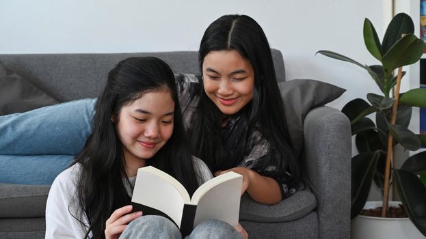 Two asian girls sitting in living room and reading book together.
