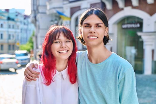 Happy couple of teenage friends hugging looking at camera, outdoor on city street. Fashion teenagers having fun together, active urban leisure, hipster youth, fun happiness joy, adolescence concept