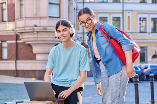 Teenage male and female using laptop for study, leisure, outdoor on city street. Guy and girl teenagers looking together at aptop screen. Lifestyle, technology, youth, education, city life concept