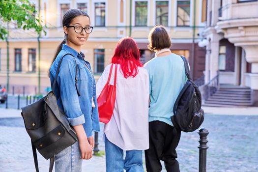 Outdoor portrait of teenage female student in city, on street. Smiling female teenager in glasses with backpack looking at camera, walking young people with back