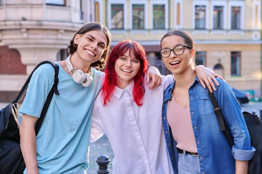 Happy smiling teenage friends hugging, looking at camera outdoor, on city street. Friendship, community, youth, lifestyle, leisure, fun concept