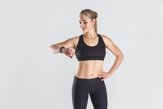 Attractive girl looking at fitness tracker and loss calories. Studio shot, gray background