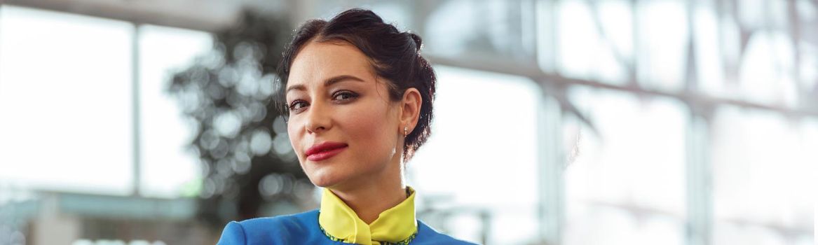 Woman airline worker wearing aviation air hostess uniform and gloves while keeping arms crossed and smiling