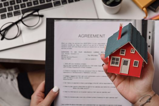 Woman holding house model and agreement contract in hand. Real estate investment and insurance concept.