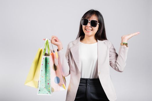 Happy woman with glasses shopper smile hold online shopping bags multicolor and show hand something empty for present product, excited Asian female purchase studio shot isolated on white background