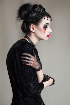 Young beautiful gothic woman with white skin and red lips with bloody drops wearing black collar with spikes. Red smokey eyes. Halloween makeup.