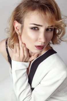 Young sexy model, posing in bra and undressing her white jacket and looking at camera. Studio shot, gray background