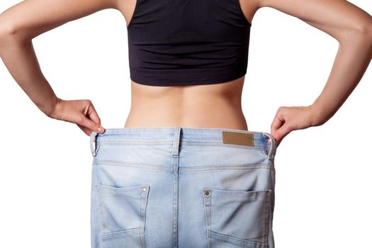 Close-up of slim waist of young woman in big jeans showing successful weight loss, isolated on white background, diet concept.