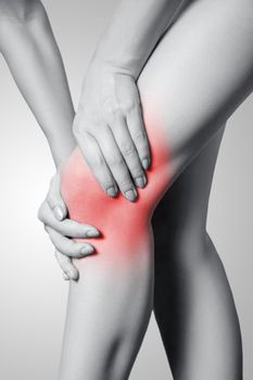 Closeup view of a young woman with knee pain on gray background. Black and white photo with red dot.