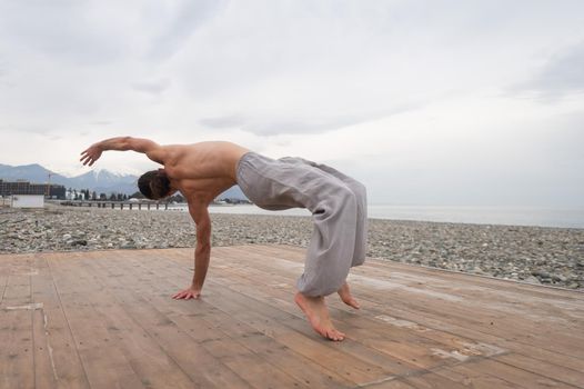 Shirtless caucasian man doing backflip on pebble beach