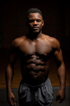 Portrait of an African American man with a naked torso in a dark studio. Muscular guy