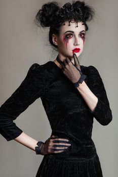 Young beautiful gothic woman with white skin and red lips with bloody drops wearing black collar with spikes. Red smokey eyes. Halloween makeup.