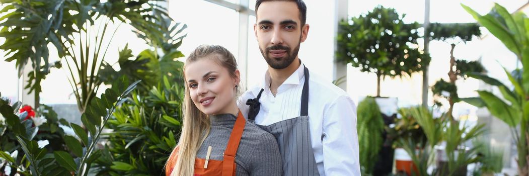 Portrait of pretty young consultants work in small flower delivery shop and sale indoor plants in pots. Business, floral design, creative studio concept