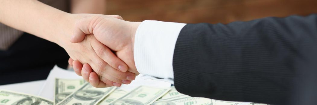 Close-up of man and woman shake hands over stack of dollars currency transaction of powers. People agreed on price. Business, big money, investment concept