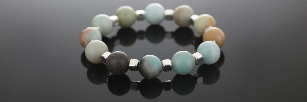 Close-up of shiny cute hand bracelet made of semiprecious stones. Real energy crystal presented on grey background with reflection. Heal, accessory concept