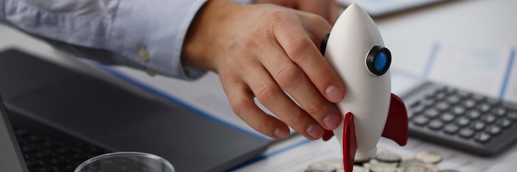 Close-up of person hold rocket model over bunch of coins and business papers on table. Launch rocket, startup, open business, risk and strategy concept