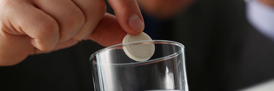 Close-up of tired man put tablet in glass with water to stop headache because of big workload. Aspirin medication to relief pain. Medicine, remedy concept