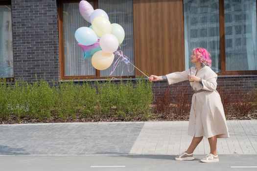 Woman in colored hair walks with an armful of balloons and drinks a refreshing beverage.