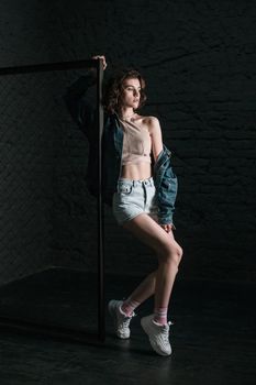 Full length profile Side view of beautiful young woman with makeup and in casual style near fance posing on dark brick wall background. indoor studio shot.