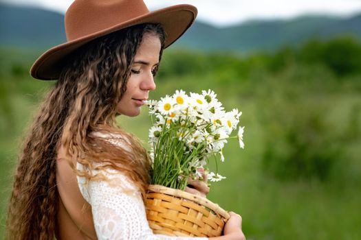 A middle-aged woman in a white dress and brown hat holds a large bouquet of daisies in her hands. Wildflowers for congratulations.