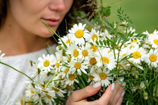 A middle-aged woman holds a large bouquet of daisies in her hands. Wildflowers for congratulations.