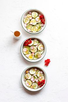 cucumber and radish cold salad served in three bowls and decorated with dill and red currants, top view