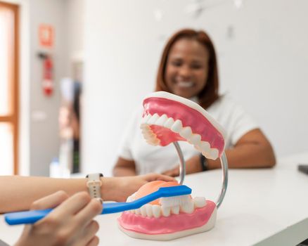 The hands of a dentist woman explaining to a black woman client the correct technique for brushing her teeth at the dental clinic