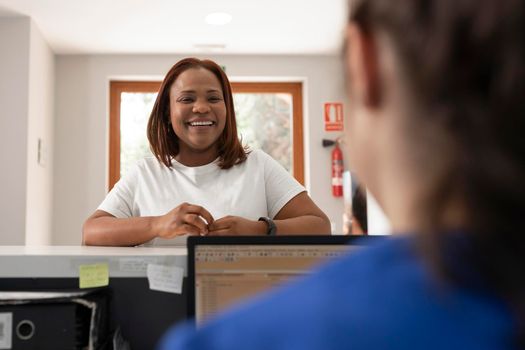 A black woman client talks with one of the employees at the counter of the dental clinic where she usually gets treated