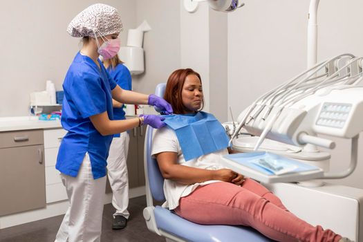 A dentist's woman assistant correctly places the tissue that prevents the client from getting any spot on her clothes at the dental clinic