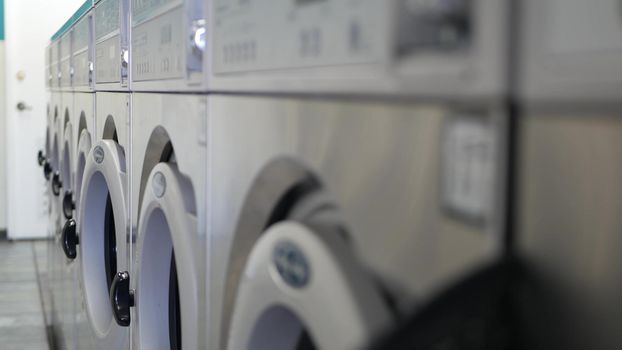 Row of washing and drying machines, public coin laundry in California, USA. Drums of washers and dryers in self-service laundromat or commercial laundrette. Automatic launderette in United States.