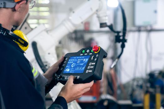 Young factory worker working with adept robotic arm in a workshop . Industry robot programming software for automated manufacturing technology .