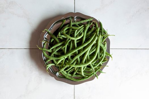 raw green beans on a metal tray on marble background, top view