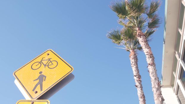 Pedestrian and bike crossing warning yellow road sign on city street, California, USA. Palm trees and sky. Ped and bicycle xing caution or attention signage. Traffic safety for bicyclist or bikers.