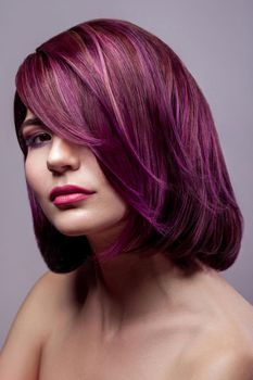 Portrait of beautiful fashion model woman with short purple colored hairstyle and makeup looking at camera. indoor studio shot, isolated on gray background.