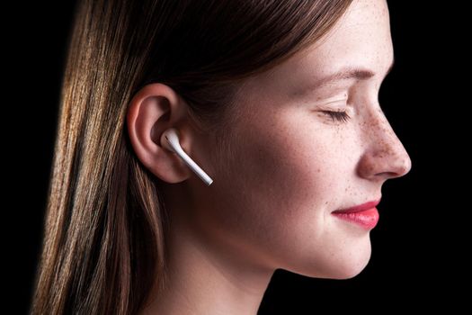 Young beautiful woman with freckles and wireless earphones on her ears. studio shot on black background..
