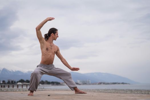 Caucasian man with naked torso practicing wushu on the seashore