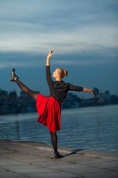 Beautiful blond young woman with black and red costume doing the splits near water. .