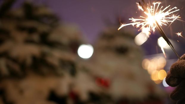 Sparkler firework burning, Christmas tree in snow, New Year or Xmas bengal light. Decorated spruce, pine or fir in snowflakes . Winter holiday fairy magic, sparkles glow, flakes and golden stars bokeh