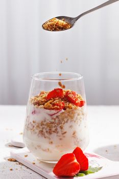 Granola seeds are poured into a glass with strawberry yogurt. Healthy breakfast. Vertical photo.