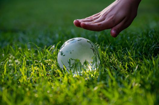 Close-up of a crystal globe and female hand on a green lawn